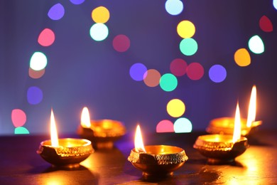 Photo of Diwali celebration. Diya lamps on dark table against blurred lights