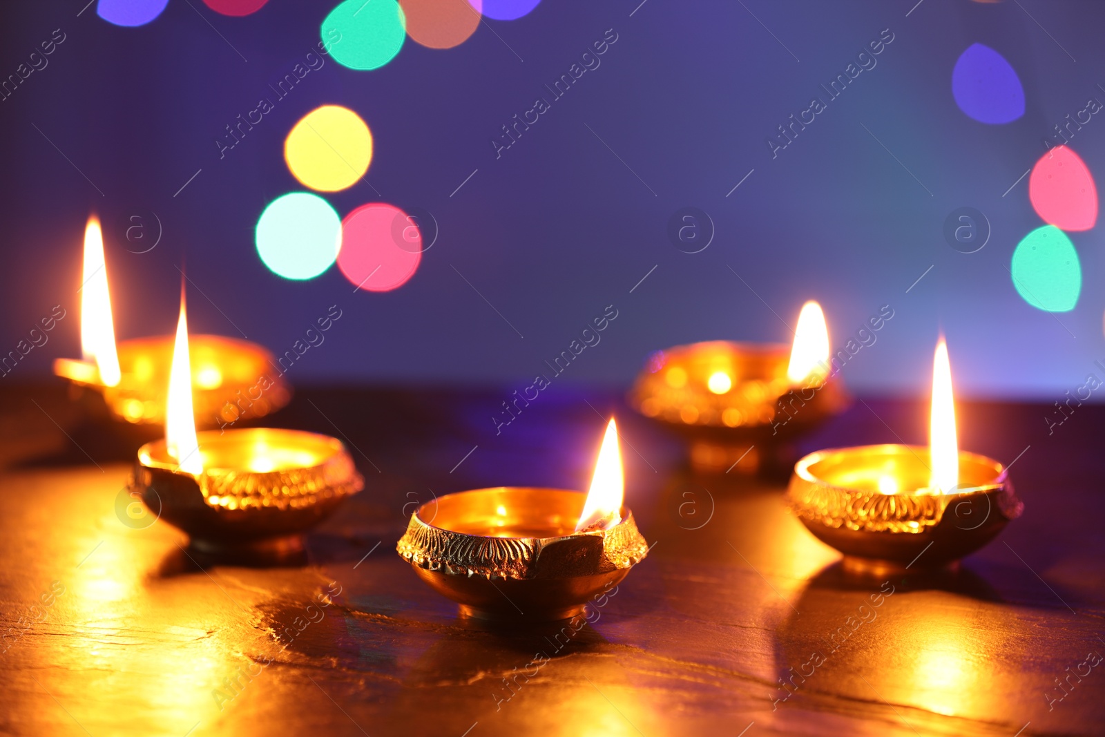 Photo of Diwali celebration. Diya lamps on dark table against blurred lights