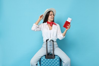 Photo of Happy young woman with suitcase, passport and ticket on light blue background