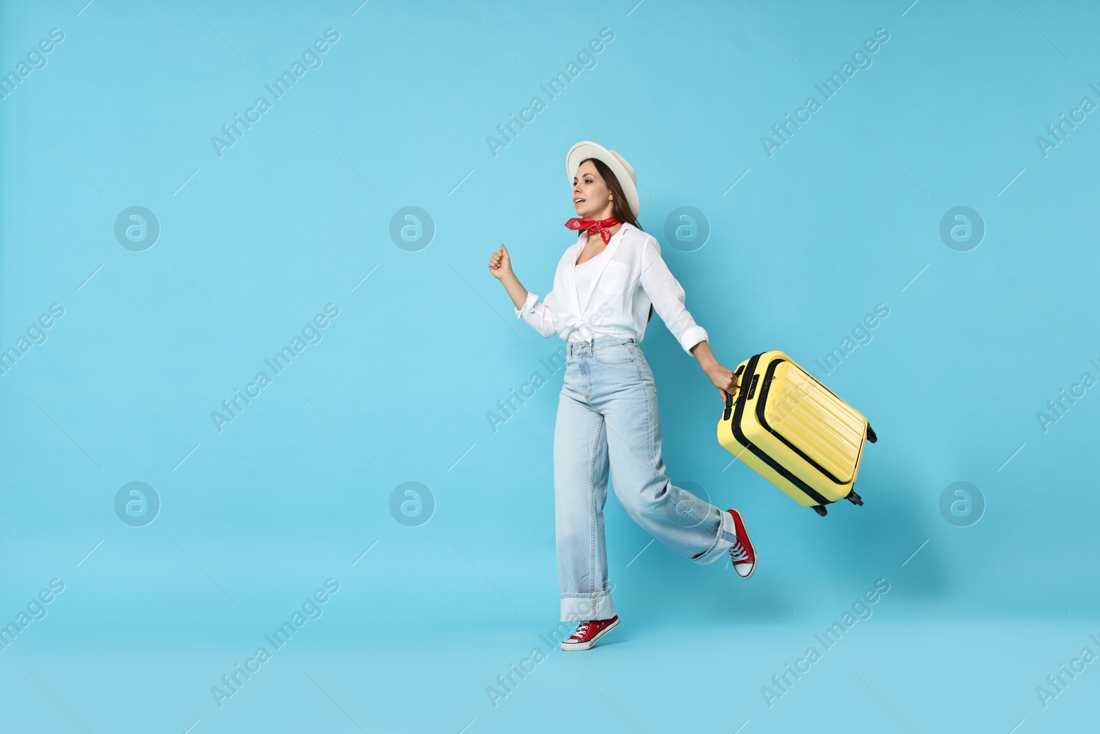 Photo of Happy young woman with suitcase on light blue background