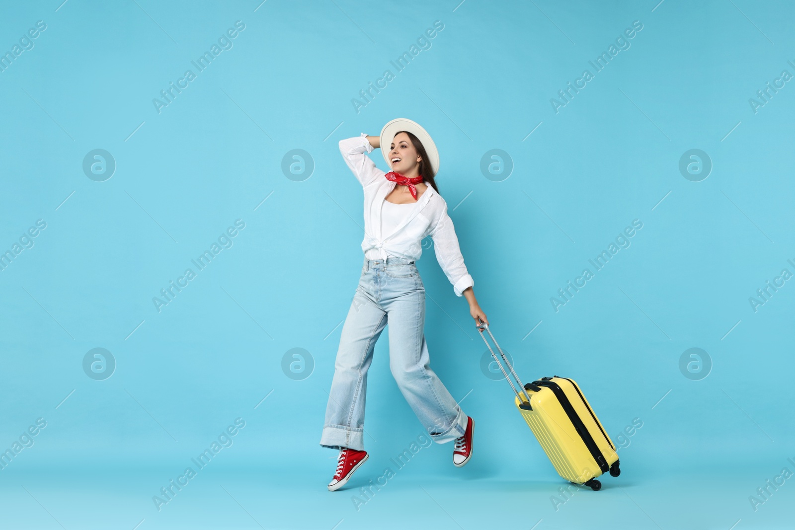 Photo of Happy young woman with suitcase on light blue background