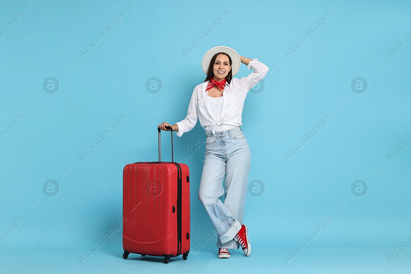 Photo of Happy young woman with suitcase on light blue background