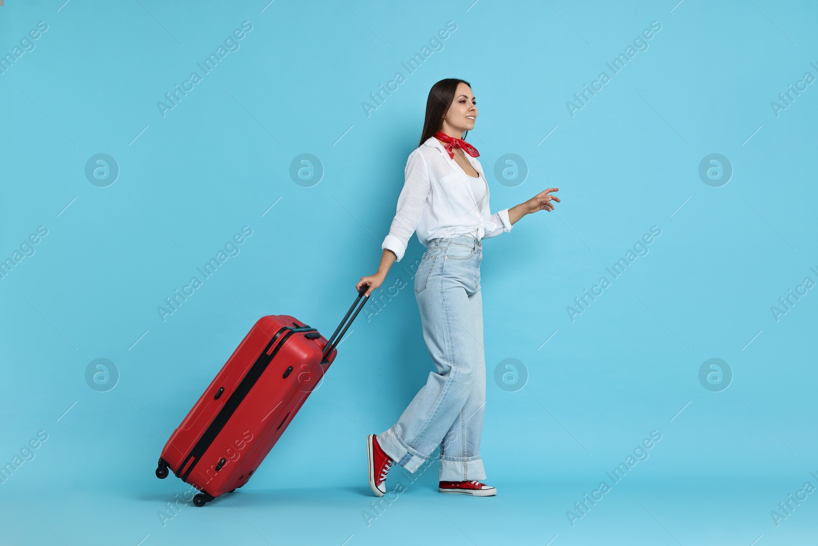 Photo of Happy young woman with suitcase on light blue background