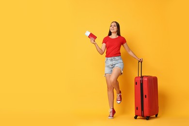 Happy young woman with suitcase, passport and ticket on orange background, space for text