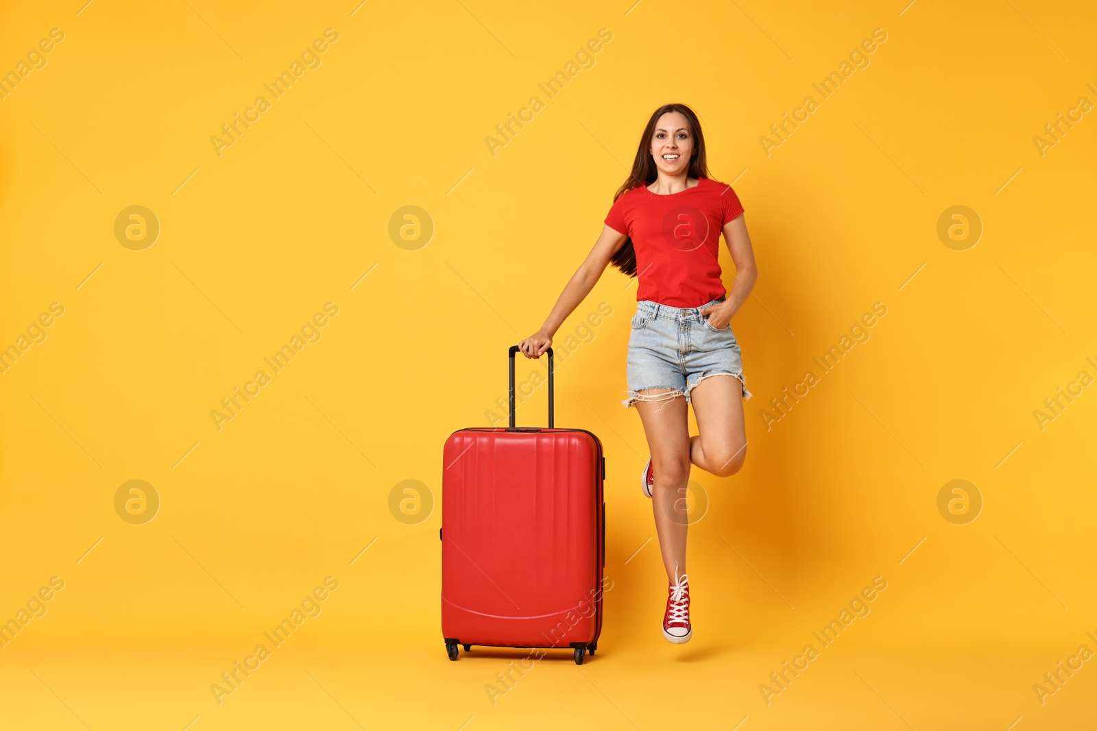 Photo of Happy young woman with suitcase on orange background