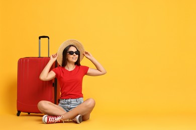 Happy young woman in sunglasses and suitcase on orange background, space for text