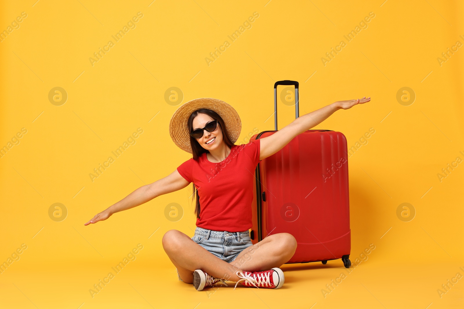 Photo of Happy young woman in sunglasses and suitcase on orange background