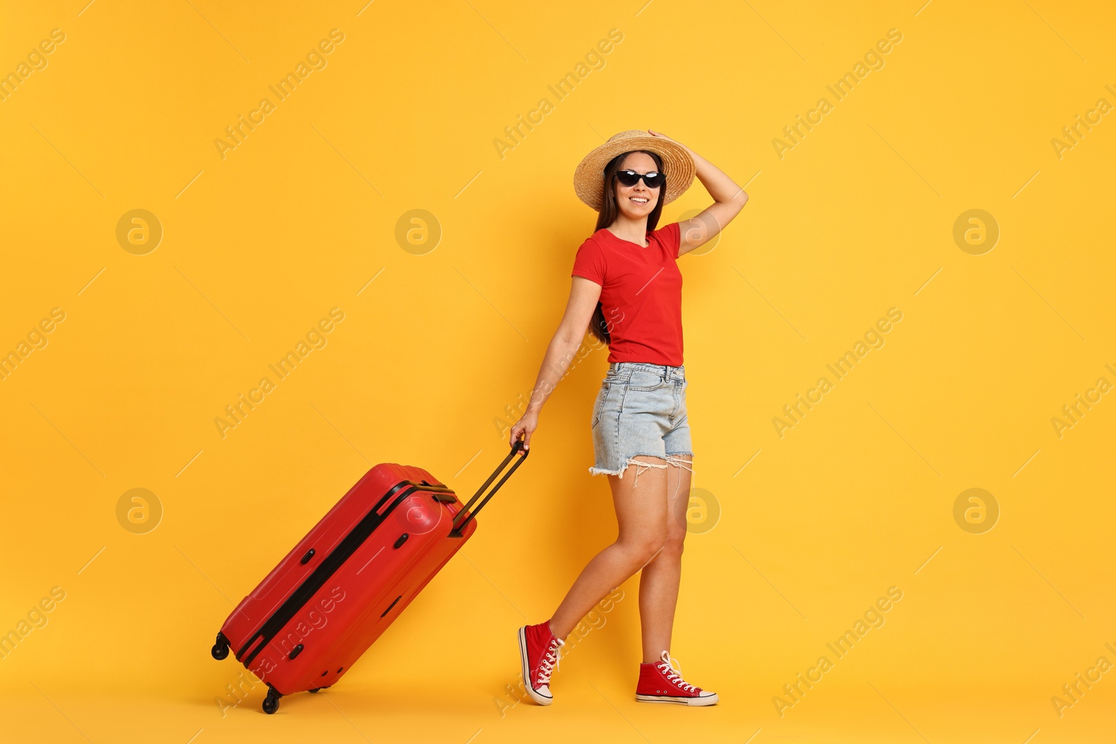 Photo of Happy young woman in sunglasses with suitcase on orange background