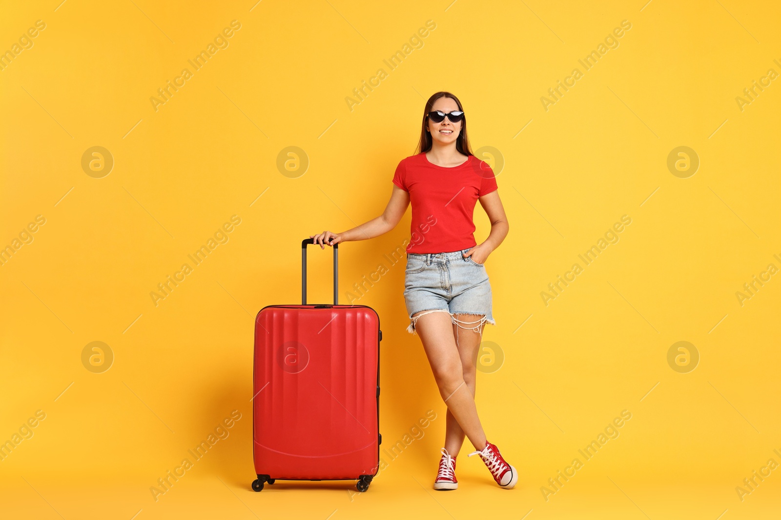 Photo of Happy young woman in sunglasses with suitcase on orange background