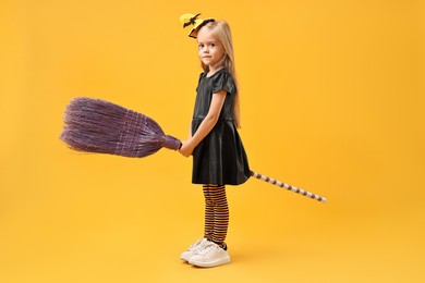 Photo of Funny girl with broom dressed like witch on yellow background. Halloween celebration