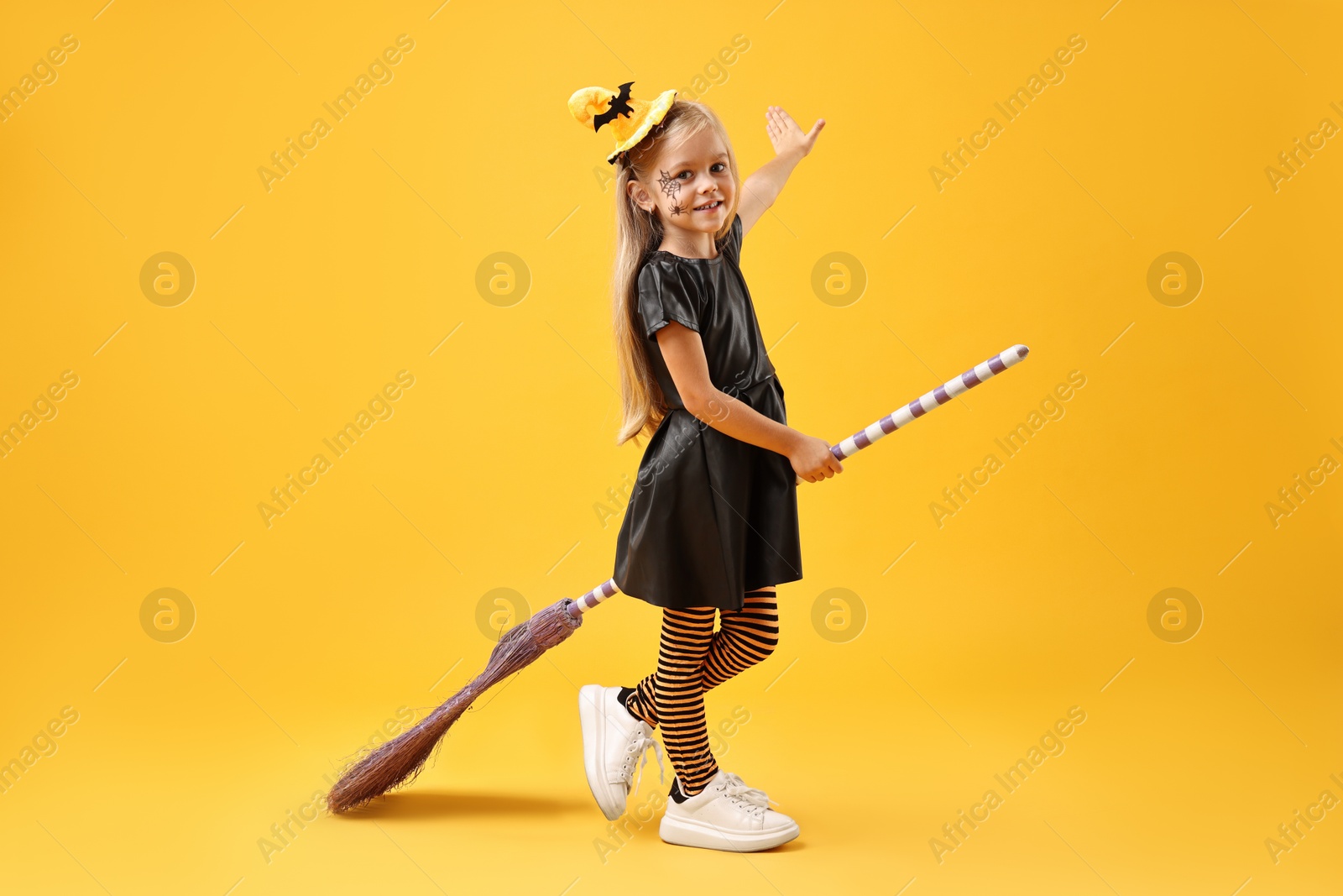 Photo of Funny girl with broom dressed like witch on yellow background. Halloween celebration