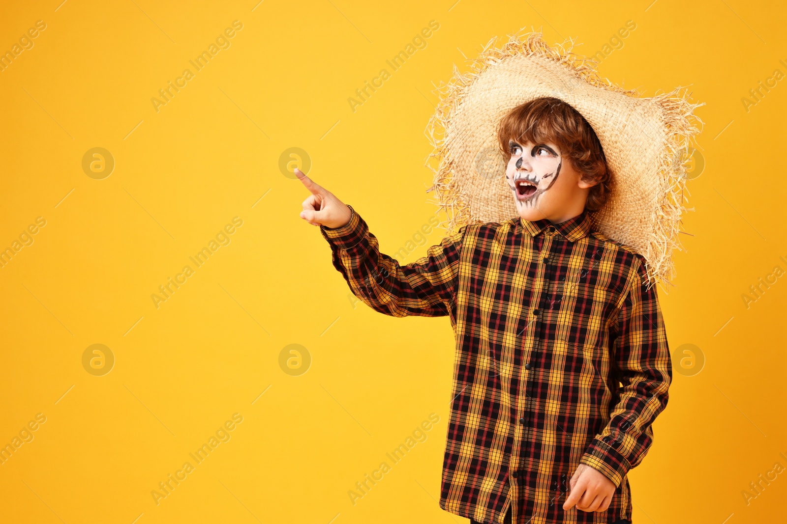 Photo of Funny boy dressed like scarecrow pointing at something on yellow background, space for text. Halloween celebration