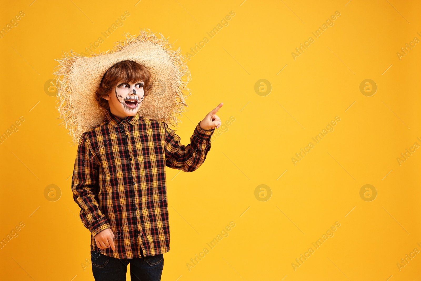 Photo of Funny boy dressed like scarecrow pointing at something on yellow background, space for text. Halloween celebration