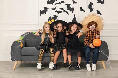 Cute children with pumpkin bucket wearing costumes indoors. Halloween celebration