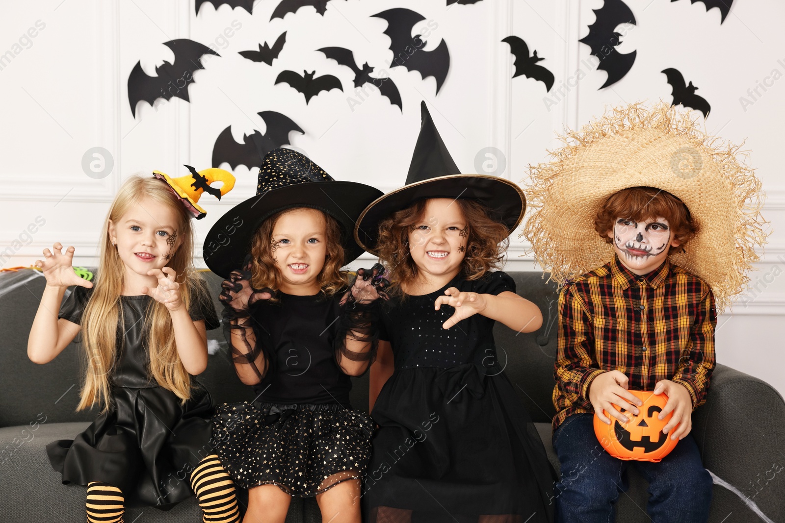 Photo of Cute children with pumpkin bucket wearing costumes indoors. Halloween celebration