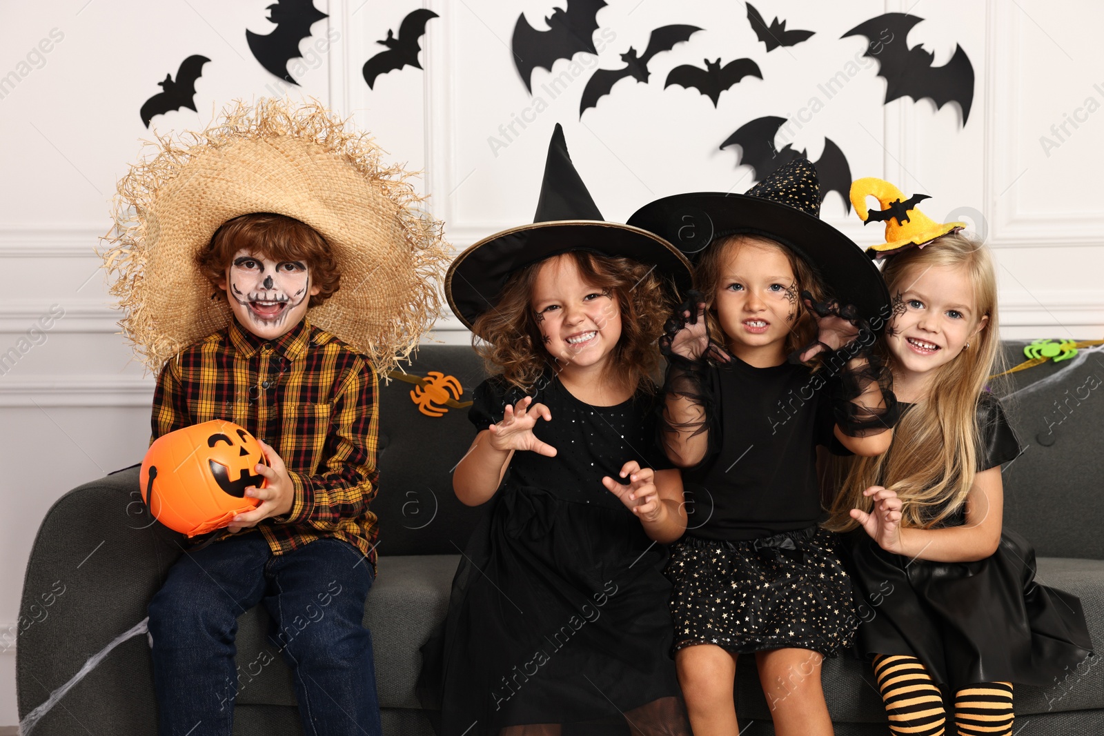 Photo of Cute children with pumpkin bucket wearing costumes indoors. Halloween celebration