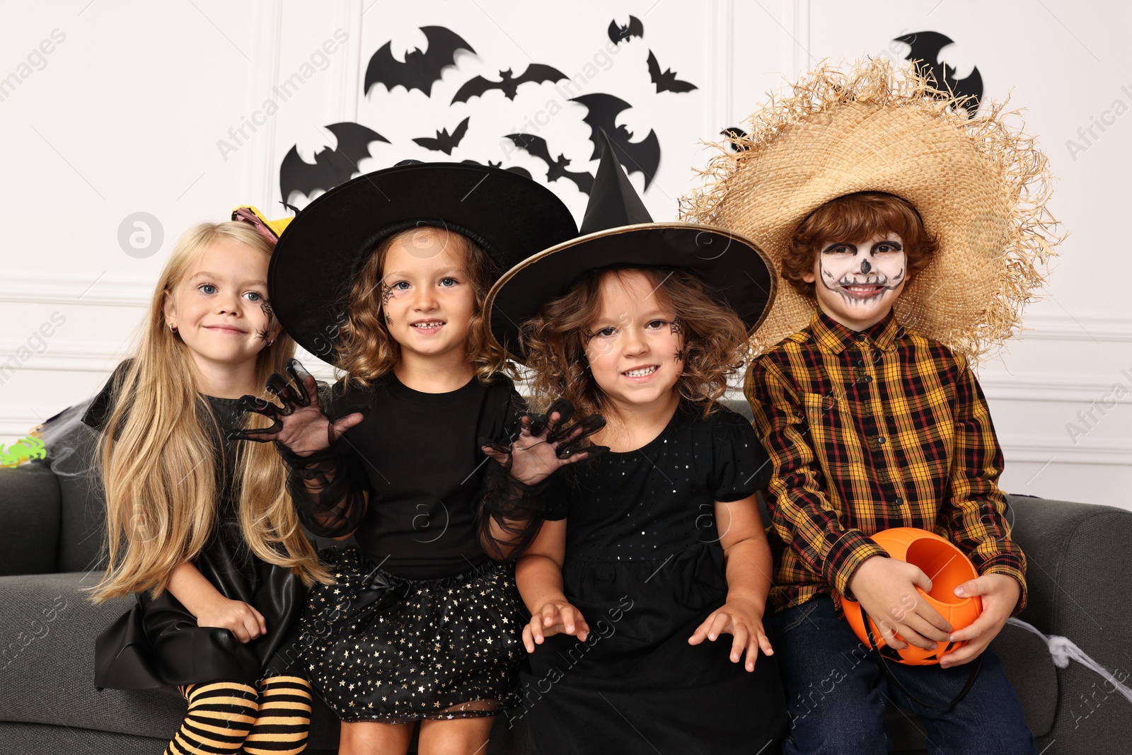 Photo of Cute children with pumpkin bucket wearing costumes indoors. Halloween celebration