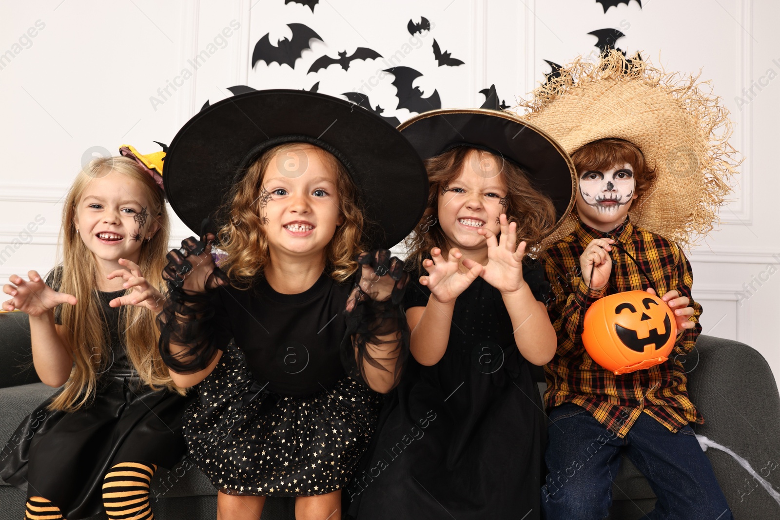 Photo of Cute children with pumpkin bucket wearing costumes indoors. Halloween celebration