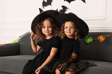 Photo of Cute girls wearing costumes on sofa indoors. Halloween celebration