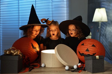 Surprised girls in costumes with festive decor and gift boxes indoors at night. Halloween celebration