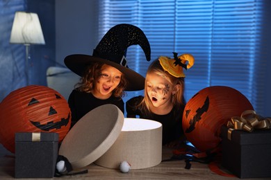 Surprised children in costumes with festive decor and gift boxes indoors at night. Halloween celebration