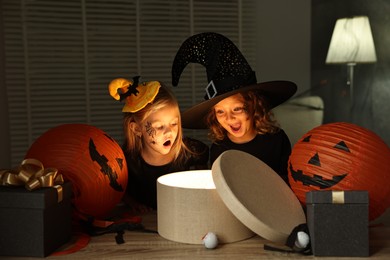 Surprised children in costumes with festive decor and gift boxes indoors at night. Halloween celebration