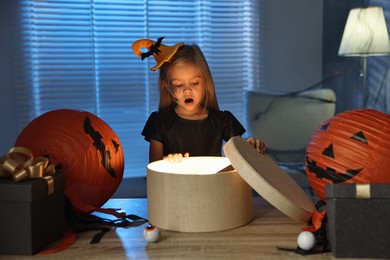 Photo of Surprised girl dressed like witch with festive decor and gift boxes indoors at night. Halloween celebration