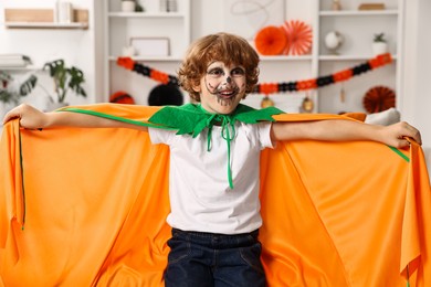 Photo of Funny boy dressed like pumpkin for Halloween celebration in room