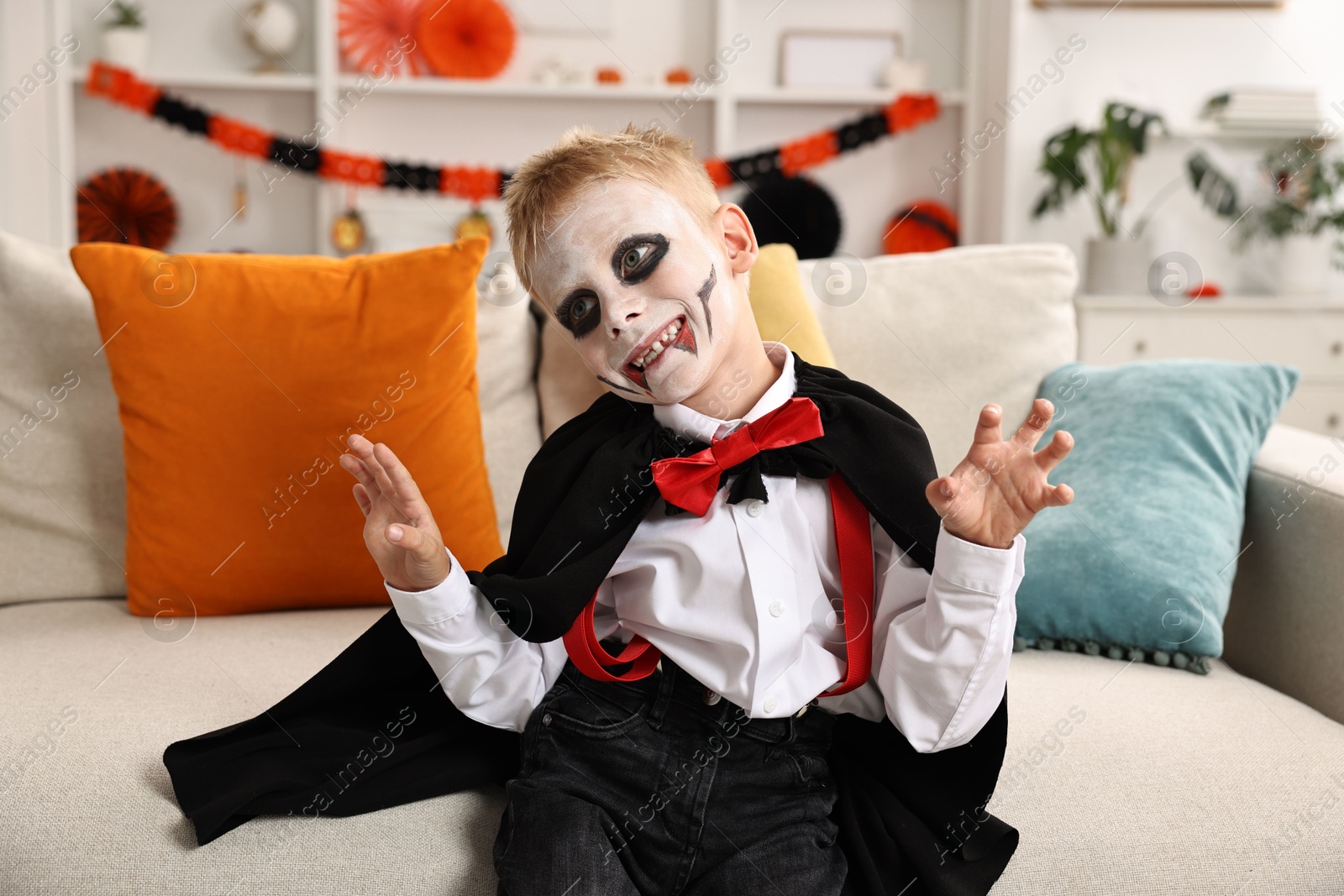 Photo of Funny boy dressed like vampire for Halloween celebration on sofa in room