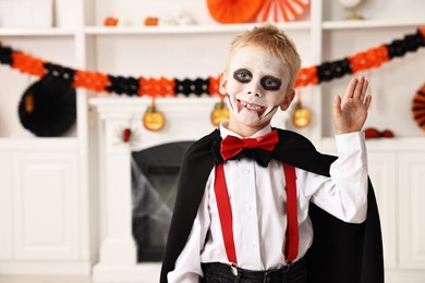 Photo of Funny boy dressed like vampire for Halloween celebration in room