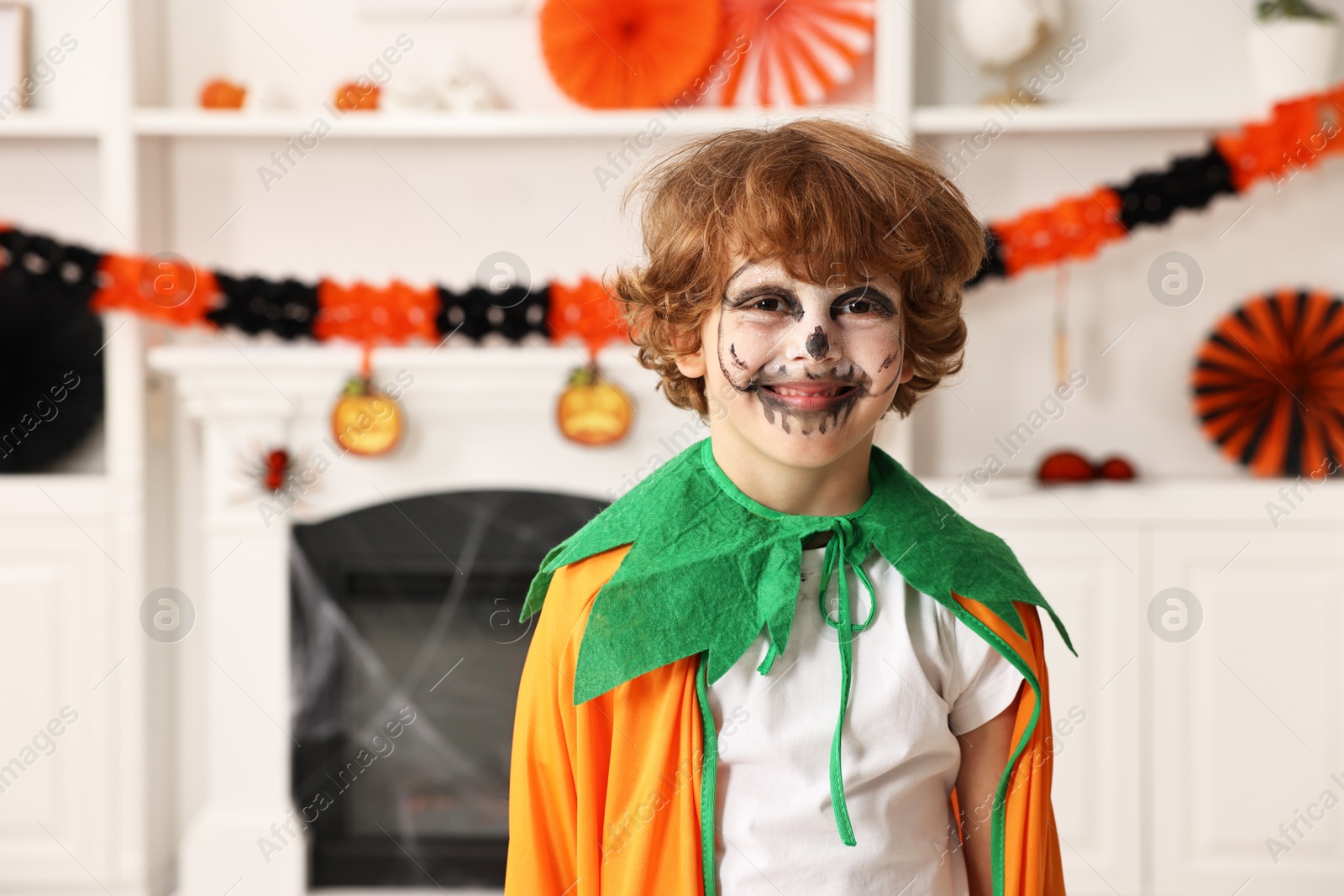 Photo of Funny boy dressed like pumpkin for Halloween celebration in room