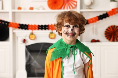 Funny boy dressed like pumpkin for Halloween celebration in room