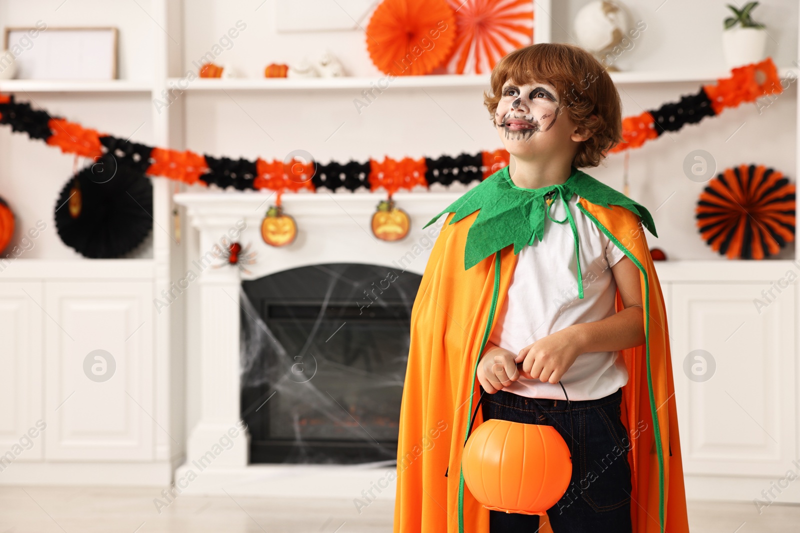 Photo of Funny boy with bucket dressed like pumpkin in room, space for text. Halloween celebration