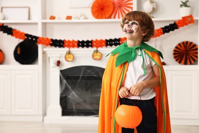 Funny boy with bucket dressed like pumpkin in room, space for text. Halloween celebration