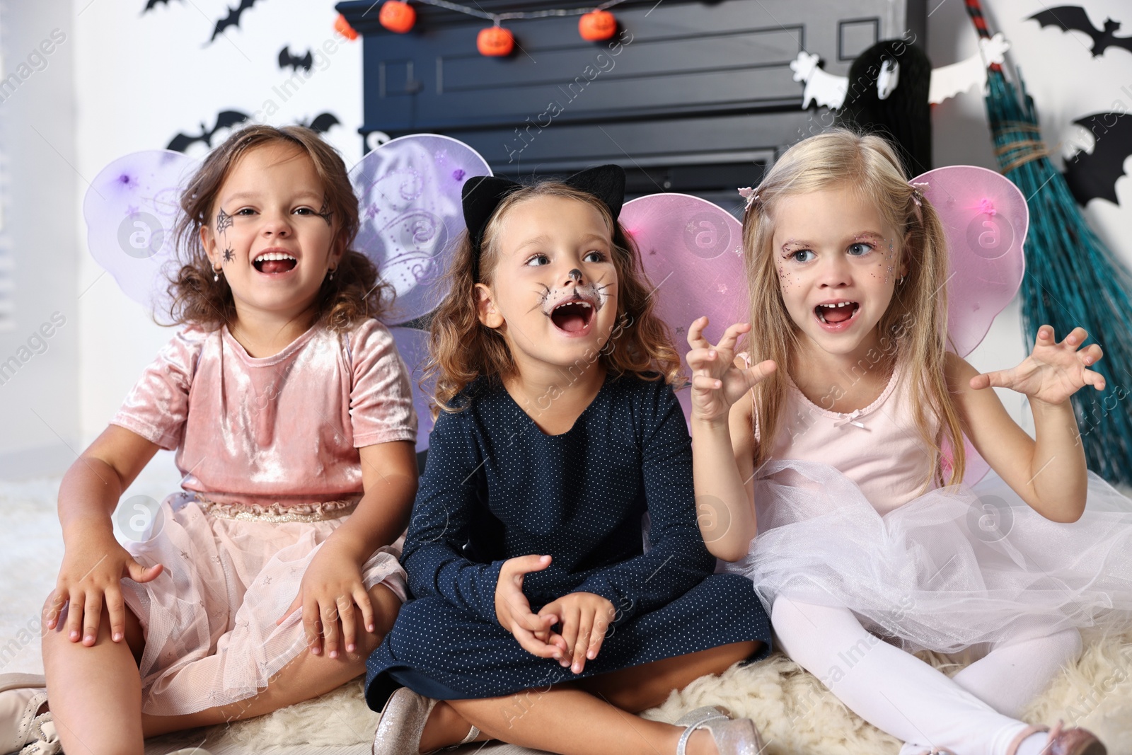 Photo of Cute girls wearing costumes for Halloween celebration in room