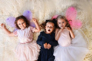 Photo of Cute girls wearing costumes on soft rug, top view. Halloween celebration