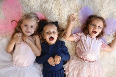 Photo of Cute girls wearing costumes on soft rug, top view. Halloween celebration