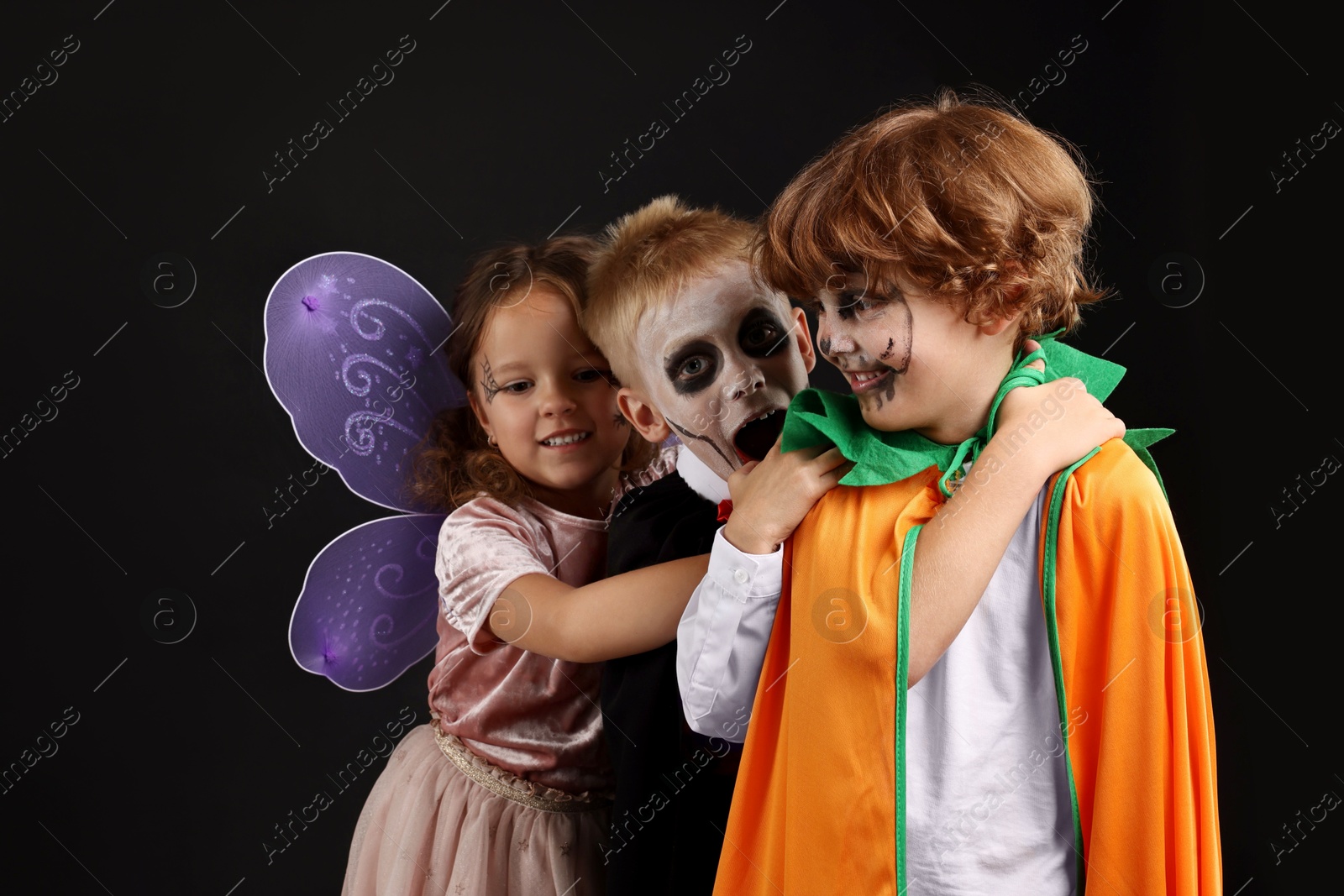 Photo of Funny children wearing costumes for Halloween celebration on black background