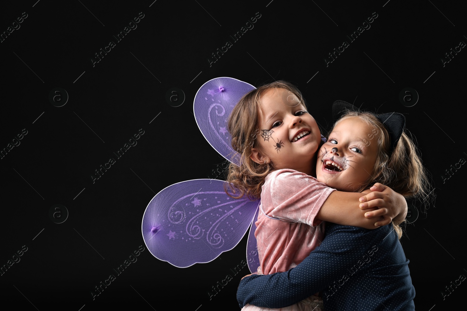 Photo of Funny girls wearing costumes on black background, space for text. Halloween celebration