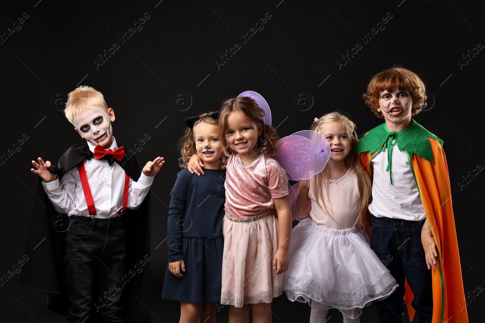 Photo of Funny children wearing costumes for Halloween celebration on black background