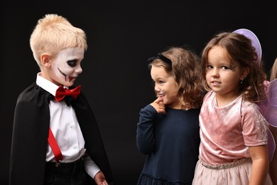 Funny children wearing costumes for Halloween celebration on black background