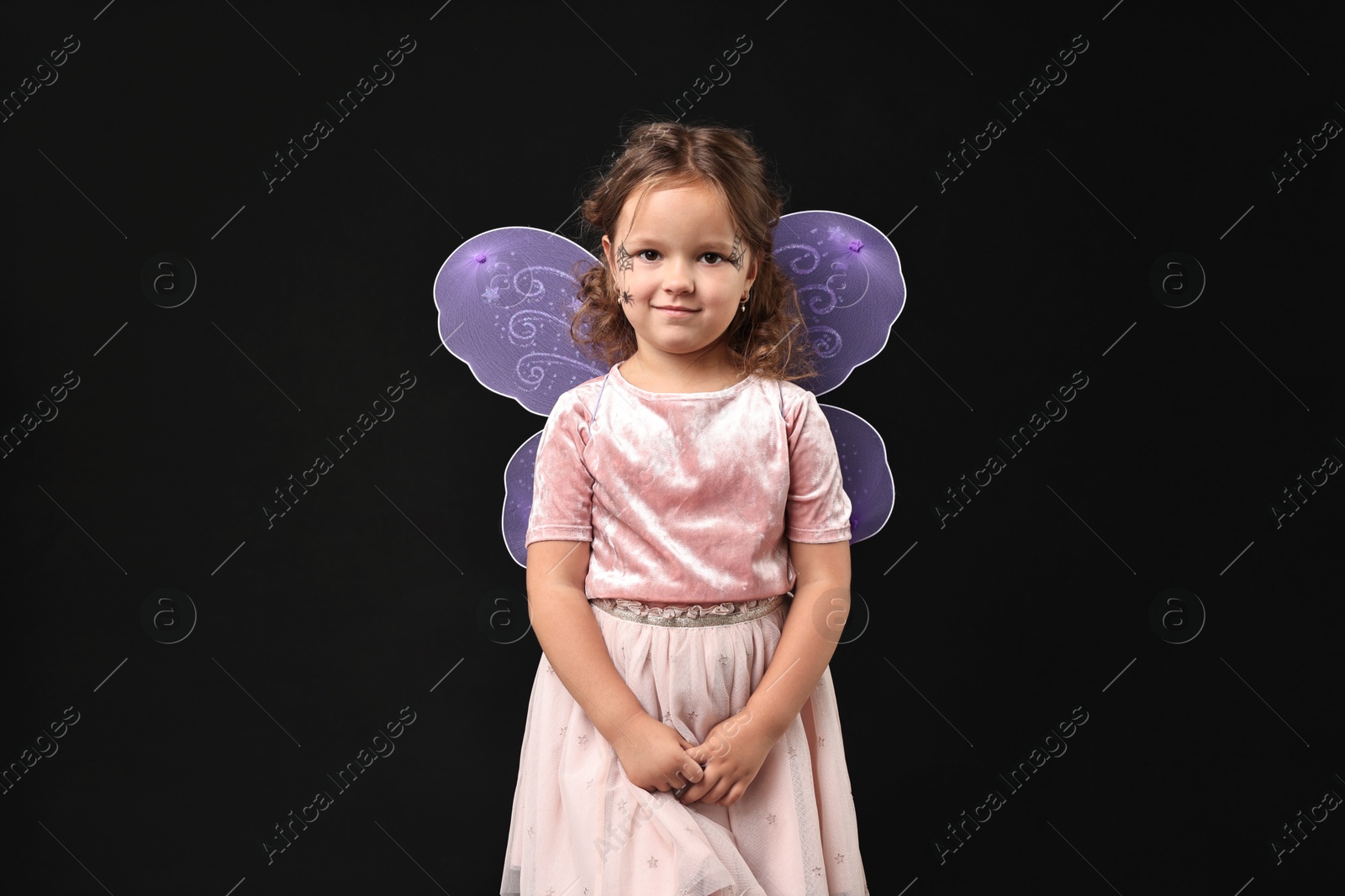 Photo of Cute girl dressed like fairy on black background. Halloween costume