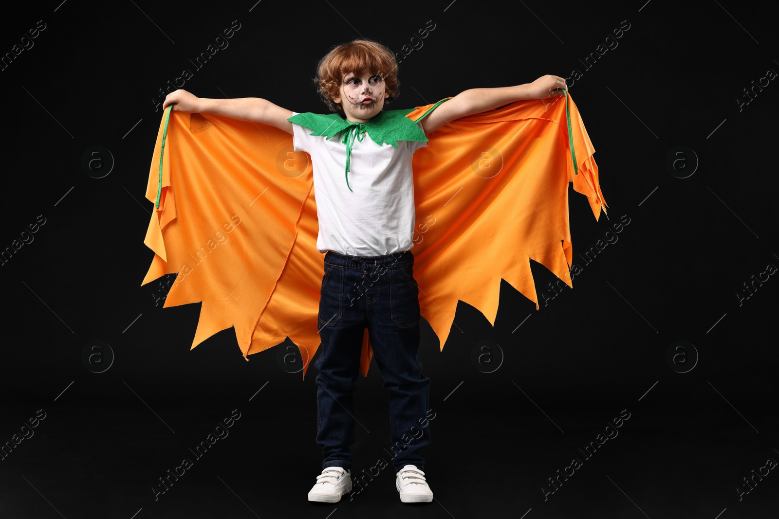 Photo of Cute boy dressed like pumpkin for Halloween celebration on black background