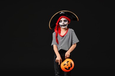 Photo of Funny boy with pumpkin bucket dressed like pirate on black background. Halloween costume