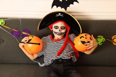 Photo of Funny boy with different Halloween decor dressed like pirate on sofa indoors