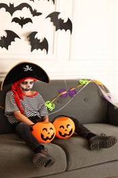 Photo of Funny boy with Halloween decor dressed like pirate on sofa indoors