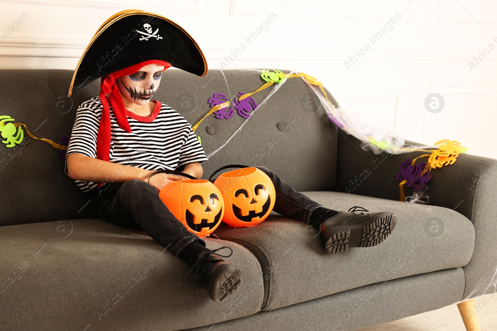 Photo of Funny boy with Halloween decor dressed like pirate on sofa indoors