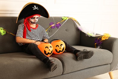 Photo of Funny boy with Halloween decor dressed like pirate on sofa indoors