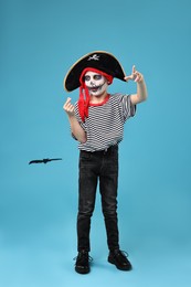 Photo of Funny boy with paper bat dressed like pirate on light blue background. Halloween costume