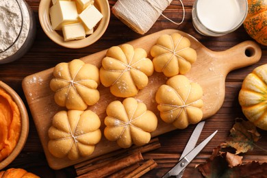 Photo of Raw pumpkin shaped buns and ingredients on wooden table, flat lay